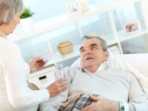 Premier Homecare Services Blog/Articles Caregiver handing medication and water to a senior man resting on the couch, part of recognizing medication side effects through close daily attention.