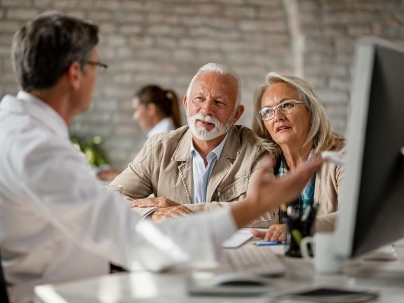 Senior couple discussing care details with a doctor at a computer, showing how appointment scheduling support helps families stay involved in every visit.