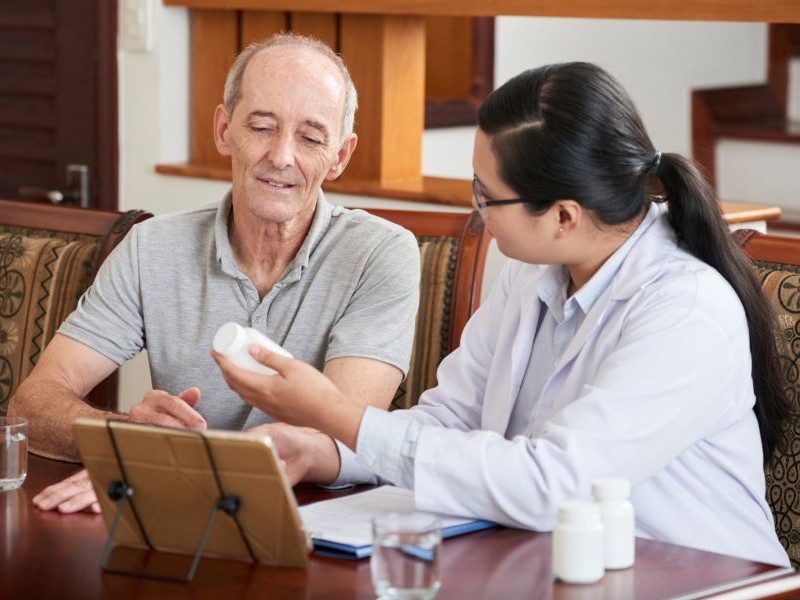 Home health provider reviewing medication with a senior man using a tablet, part of appointment scheduling support that keeps follow ups and prescriptions on track.