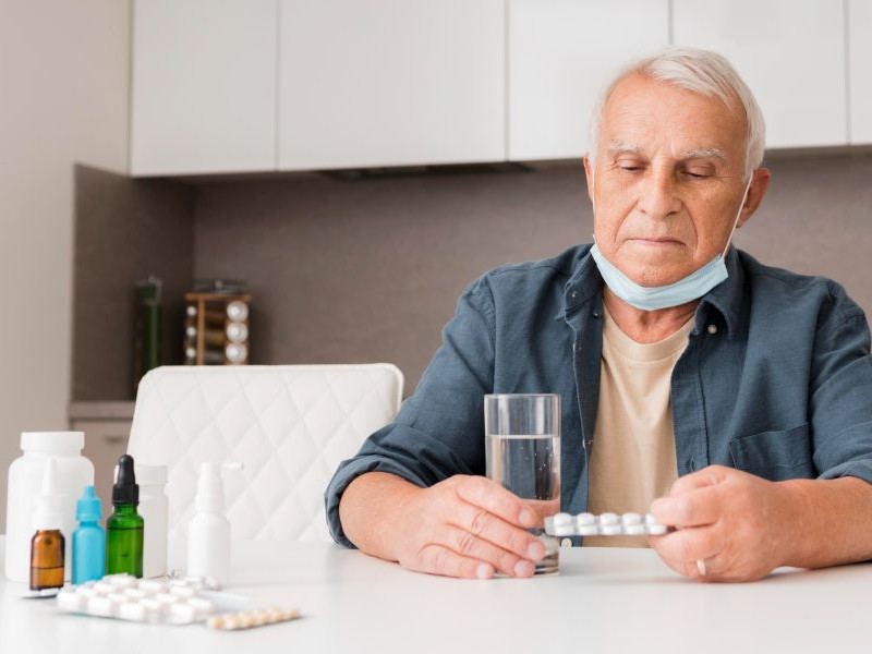 Recognizing Medication Side Effects in Seniors Senior man reviewing multiple pill packs and bottles at the table, illustrating why recognizing medication side effects matters most when managing several prescriptions.