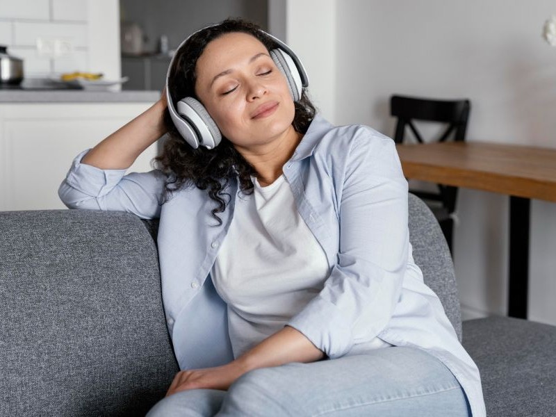 Why Preventing Caregiver Exhaustion Starts With Small Breaks Woman relaxing with headphones on the couch, preventing caregiver exhaustion by taking a quiet moment to unwind.