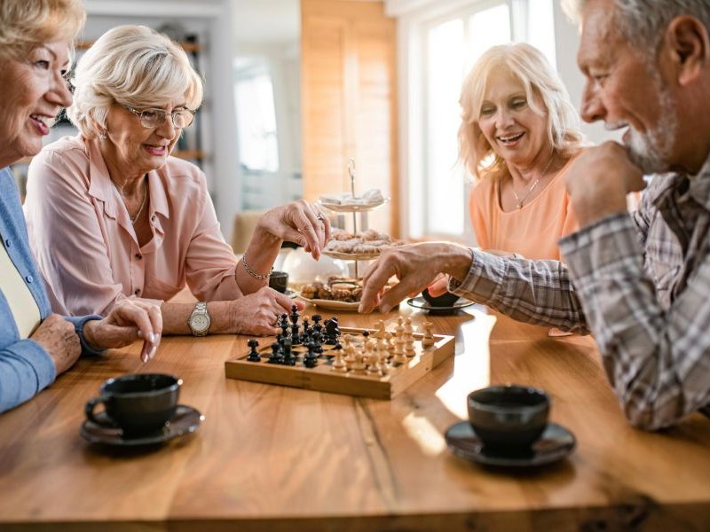 Engaging Activities for Elderly: Ideas for Quiet Afternoons Group of seniors laughing over a chess game with coffee, one of the engaging activities for elderly adults that builds focus and conversation.